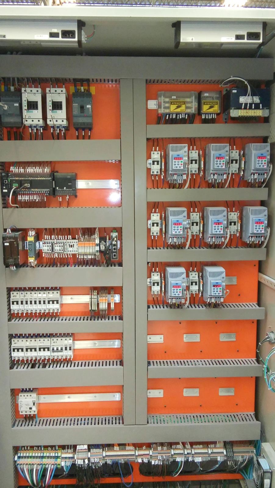 Interior de painel elétrico com acionamentos, controladores, canaletas e condutores identificados sobre placas laranja.